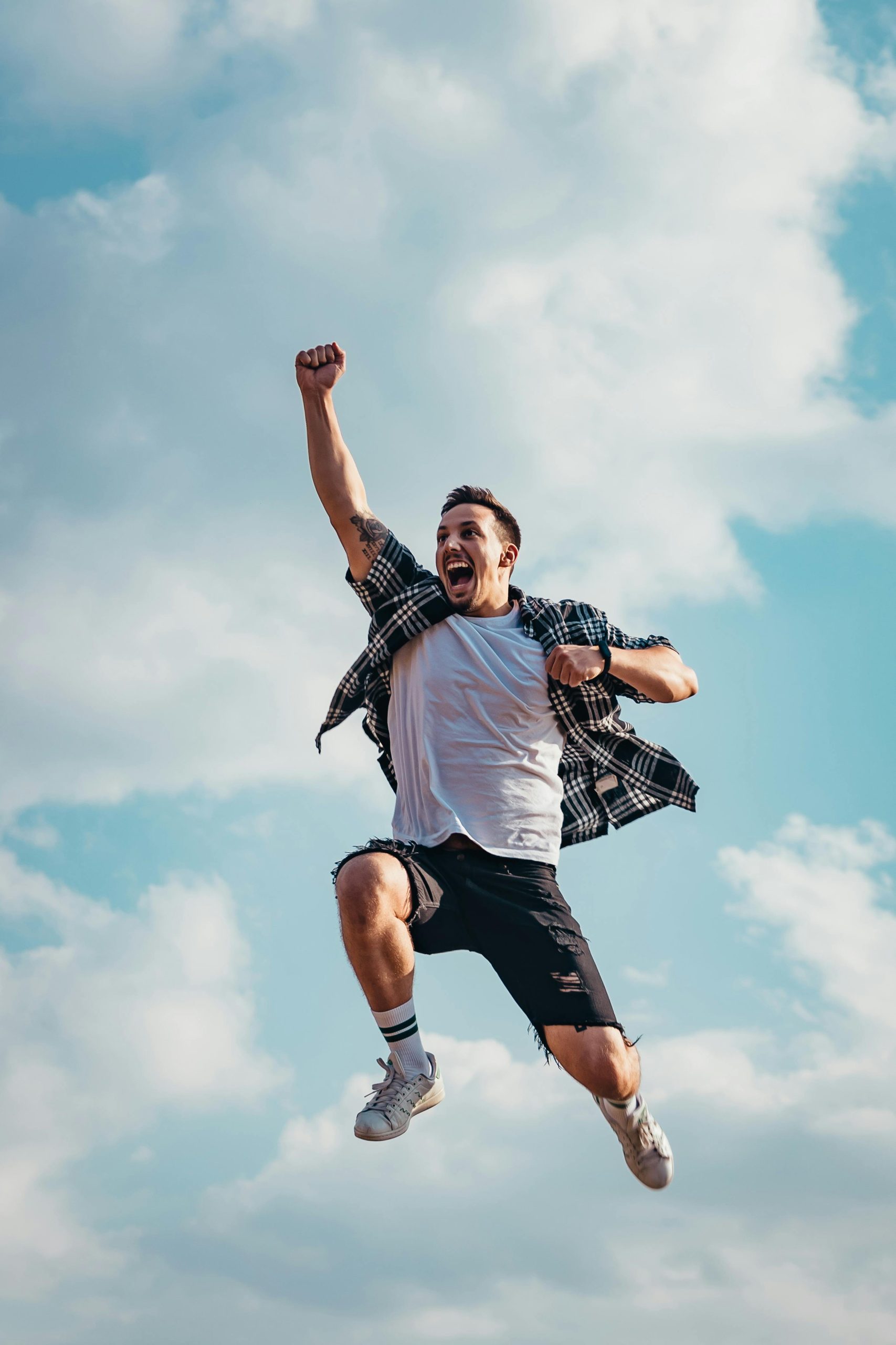 about-img A joyful young man jumps midair with clouds and blue sky in the background, exuding energy and freedom.