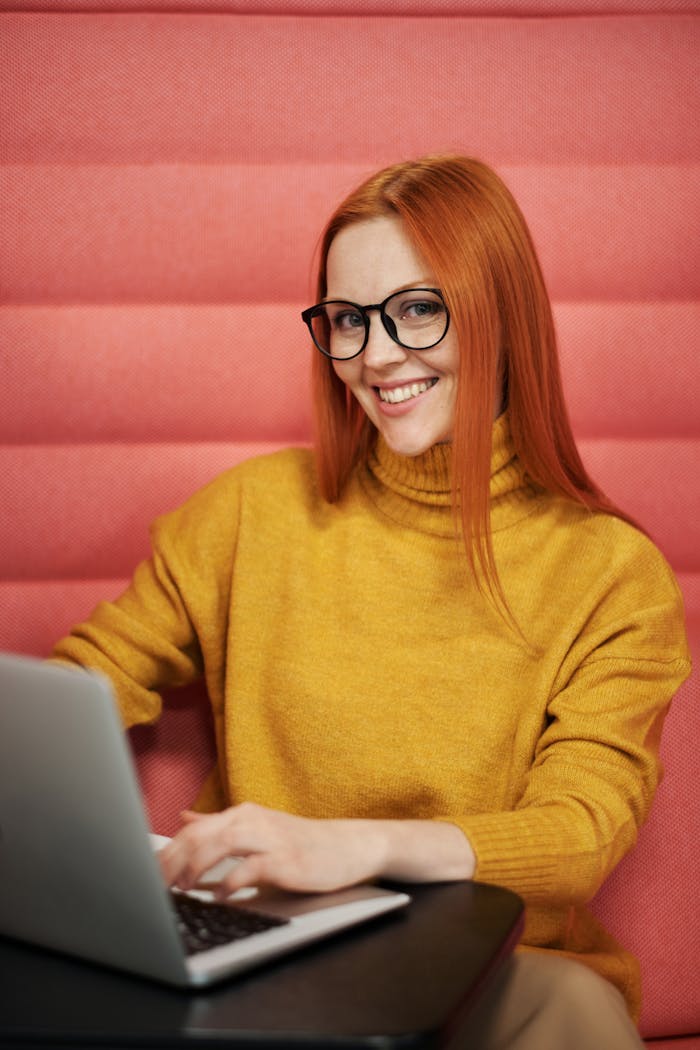Confident woman smiling while working on a laptop in a cozy indoor setting.