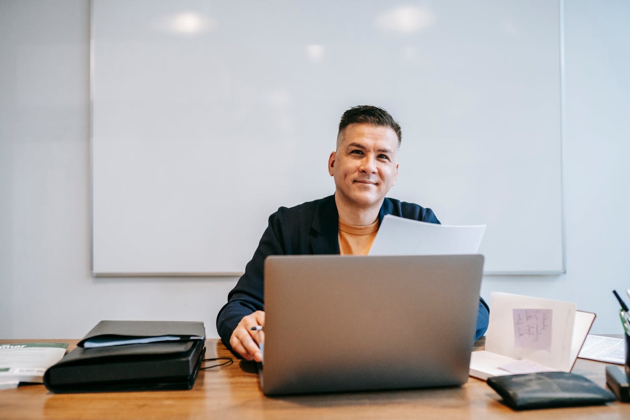 Confident man working remotely with a laptop at home office, smiling at his workspace.