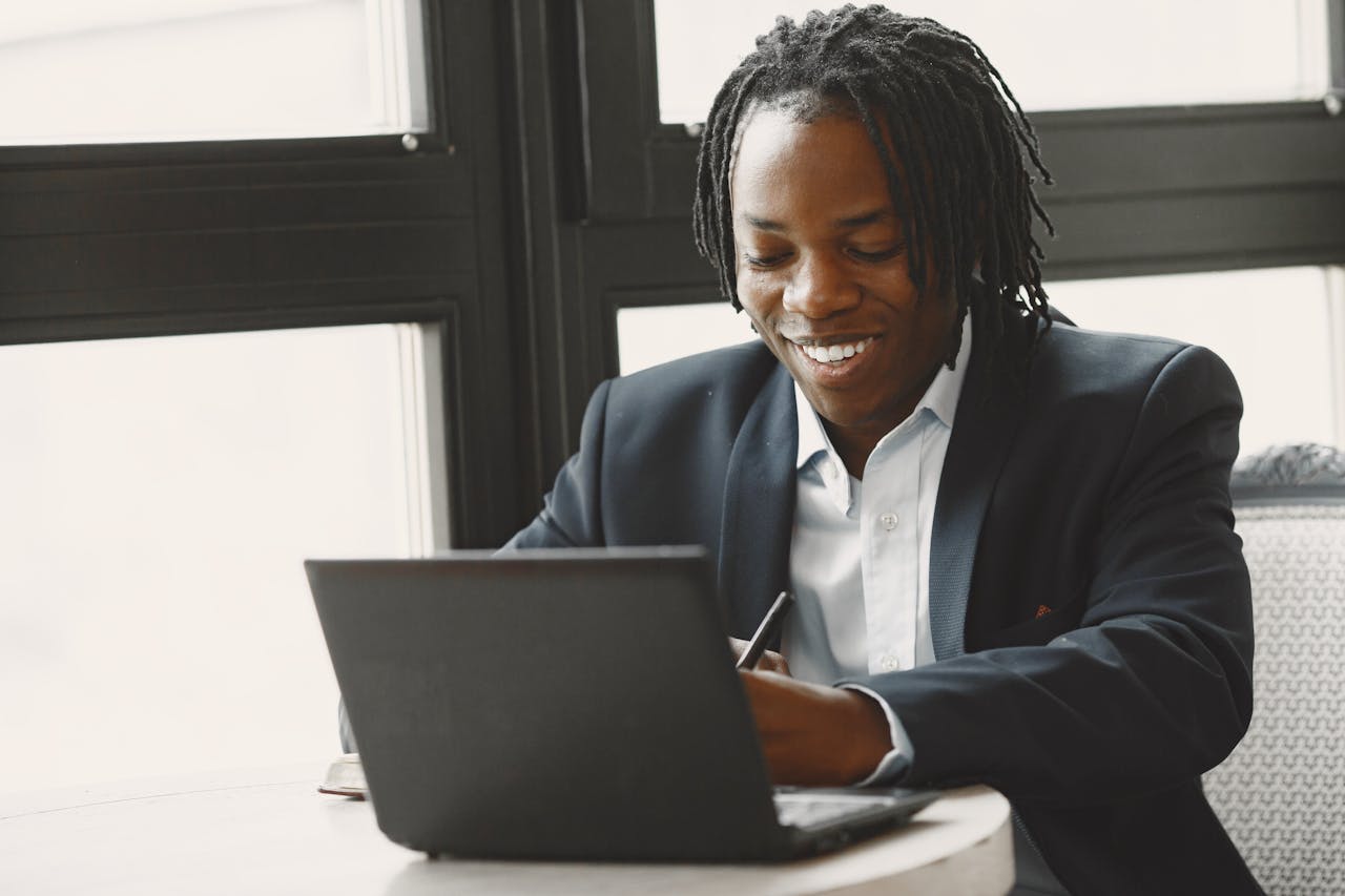 Business professional smiling and working on a laptop at a modern indoor office setting.