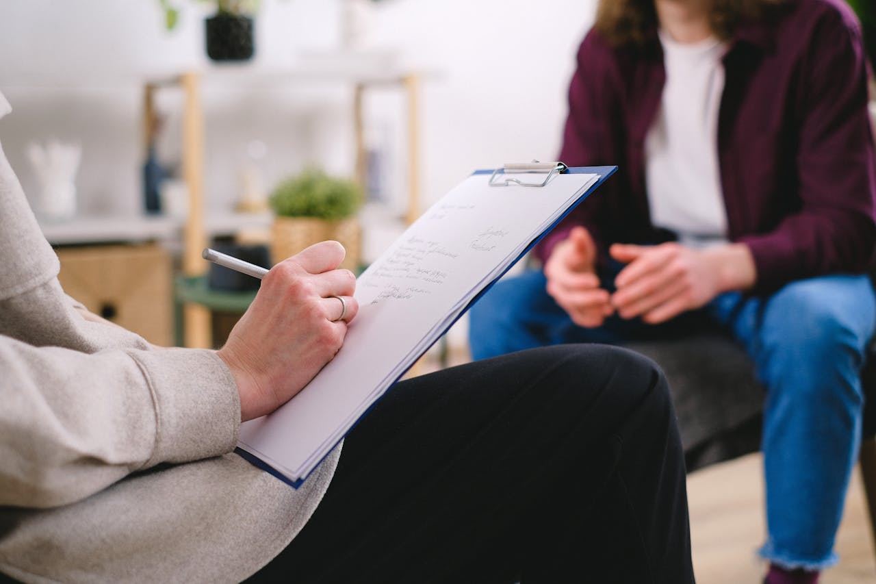 gallery-2 Close-up of a therapist writing notes on a clipboard while conversing with a patient.