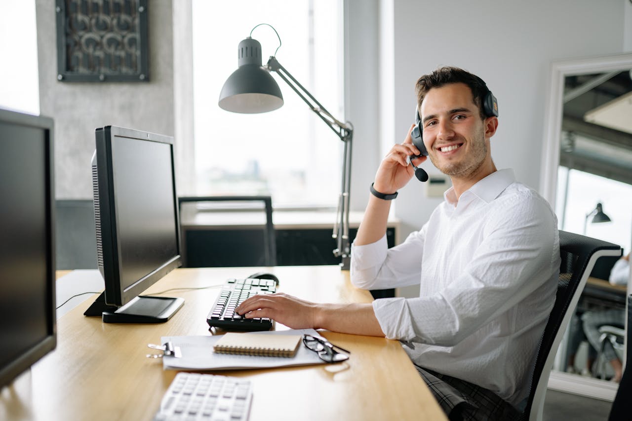 our-services-3 Smiling call center agent working at a desk with a headset and computer in a modern office.